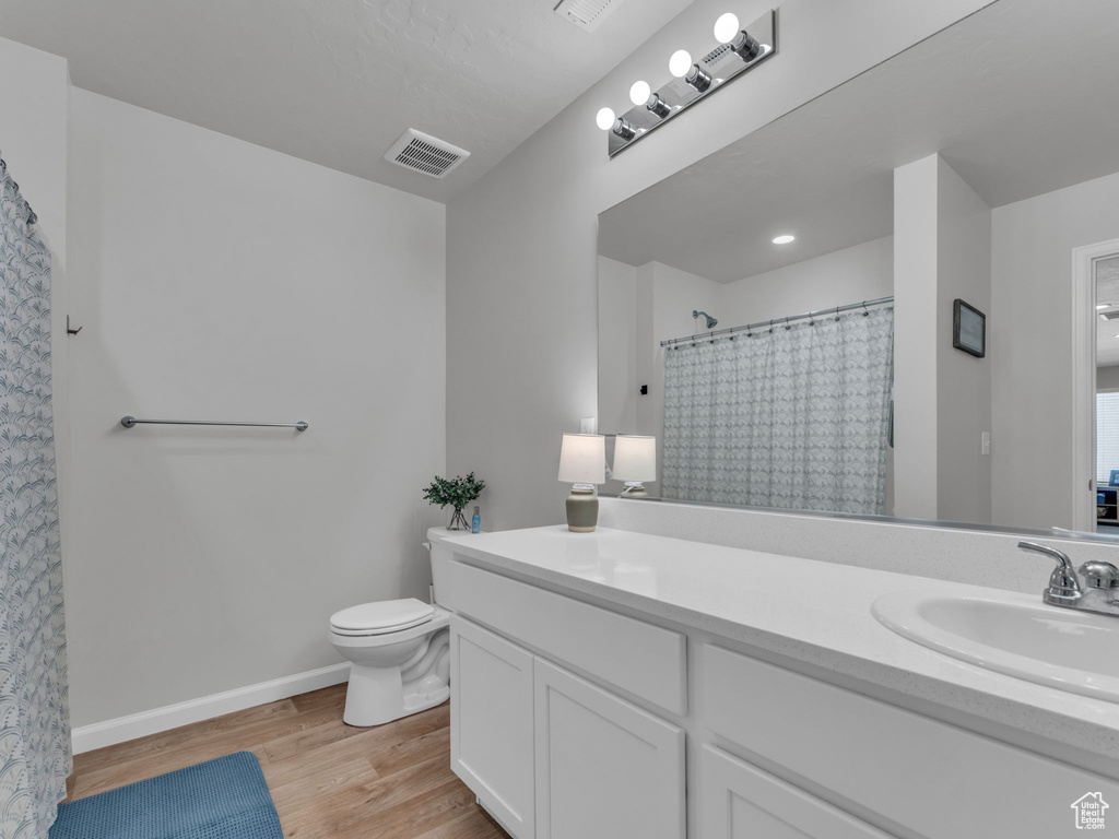 Full bath with toilet, vanity, wood finished floors, and baseboards