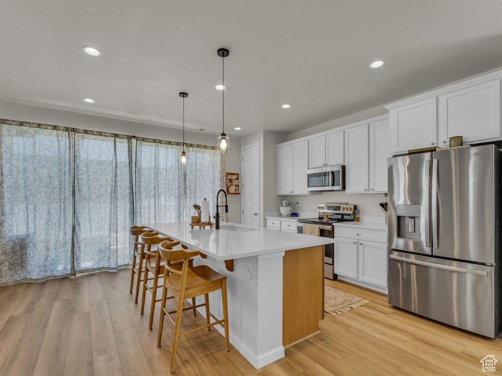 Kitchen with appliances with stainless steel finishes, a sink, light wood finished floors, light countertops, and recessed lighting