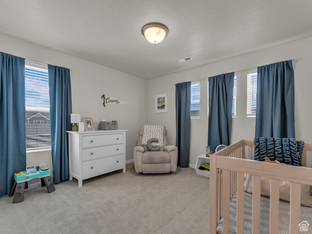 Bedroom featuring a nursery area, multiple windows, light colored carpet, and baseboards