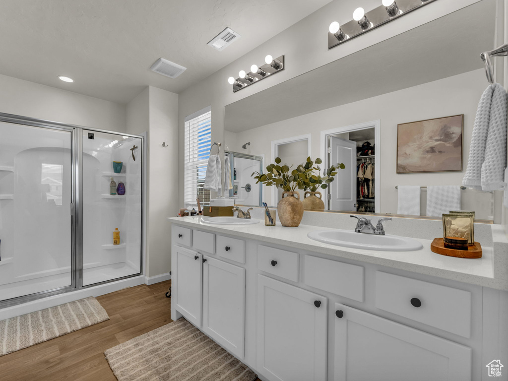 Full bath with a stall shower, double vanity, a spacious closet, wood finished floors, and recessed lighting