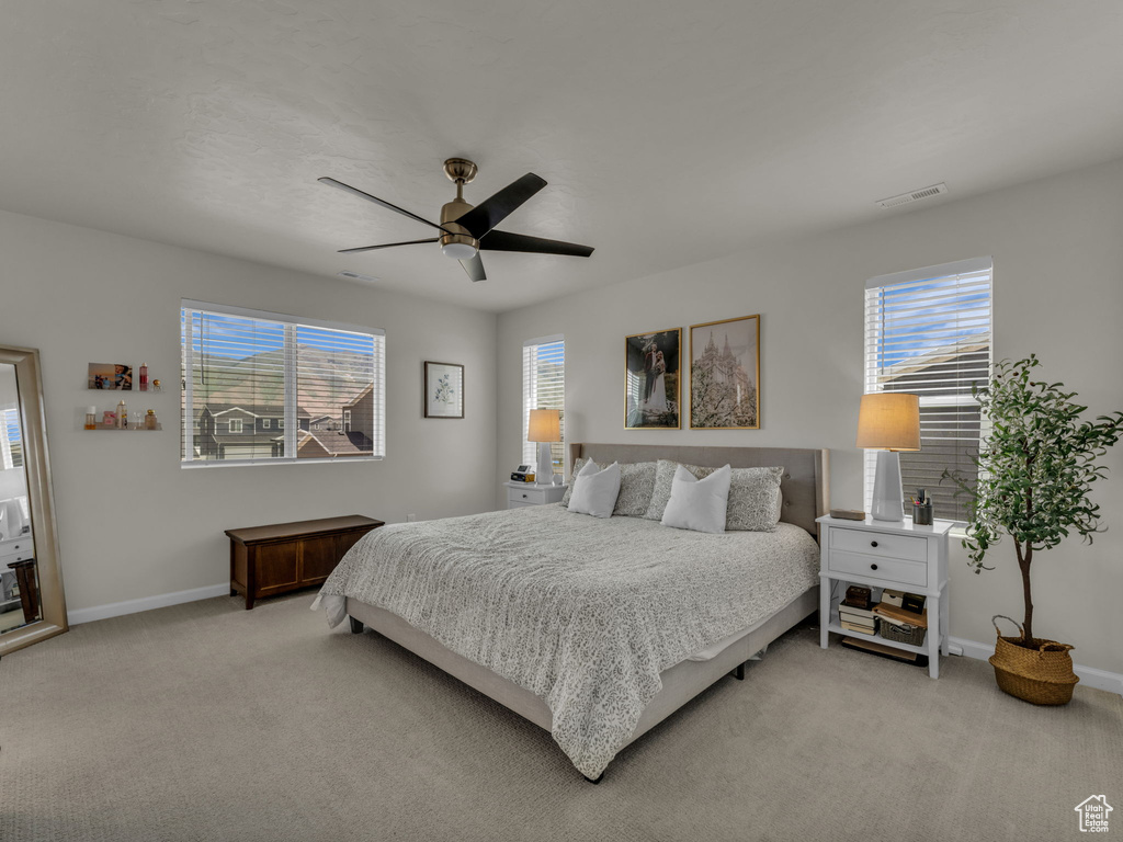 Bedroom featuring light carpet, multiple windows, baseboards, and a ceiling fan