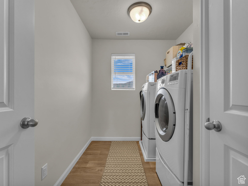Laundry area with washer and clothes dryer, light wood-type flooring, and baseboards