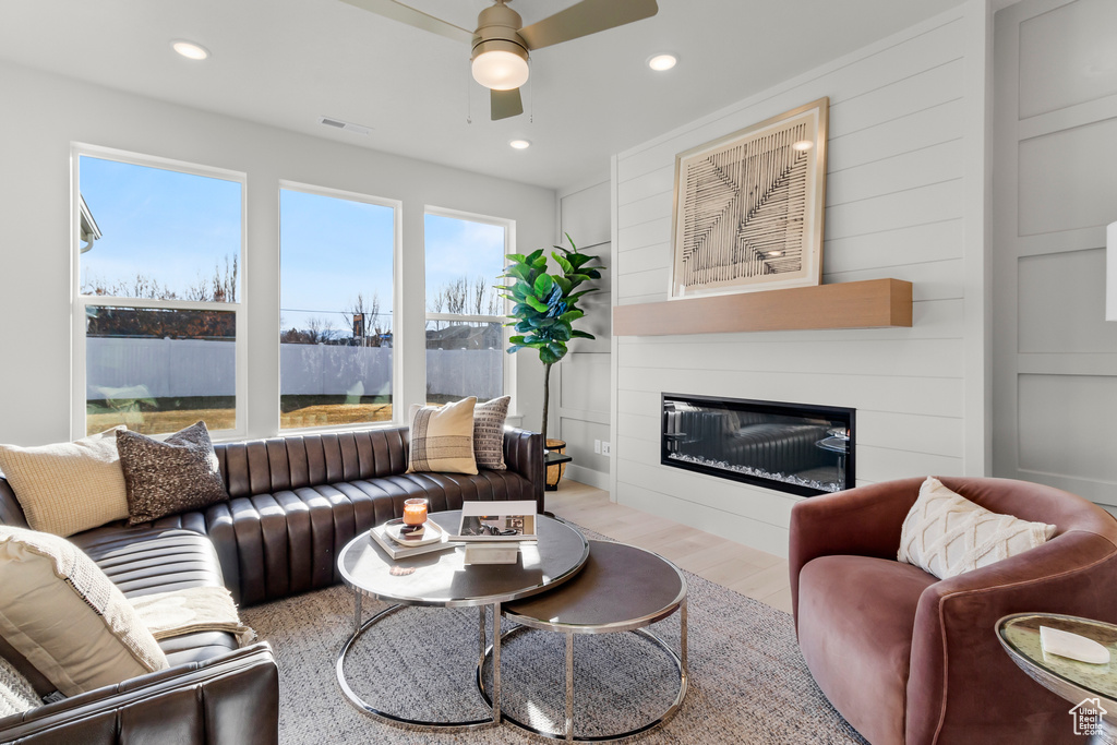 Living area with ceiling fan, a glass covered fireplace, wood finished floors, and recessed lighting