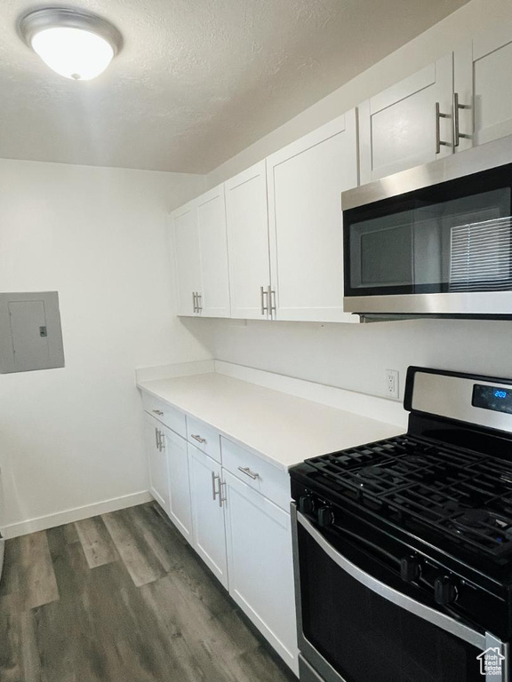 Kitchen with appliances with stainless steel finishes, electric panel, dark wood finished floors, white cabinets, and light countertops