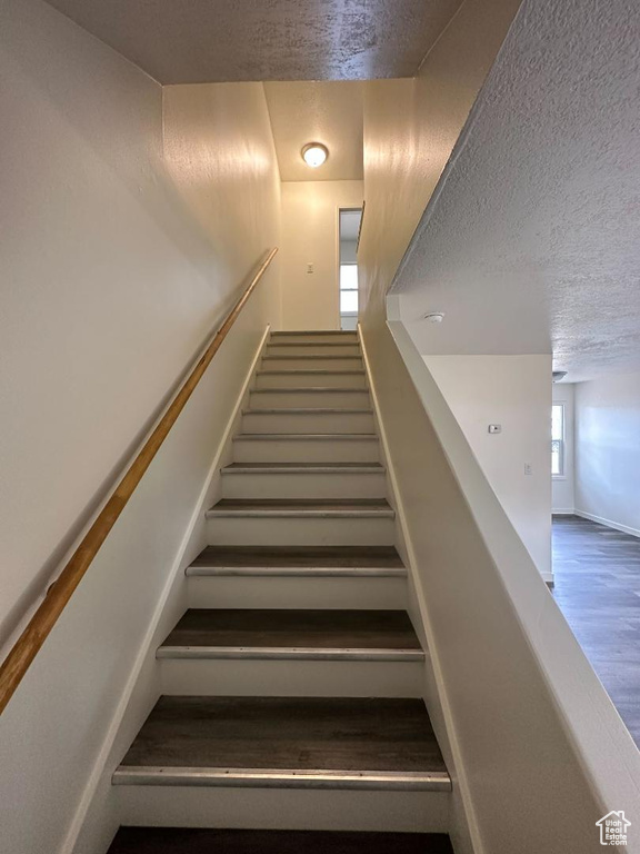 Stairs featuring a textured ceiling, wood finished floors, and baseboards