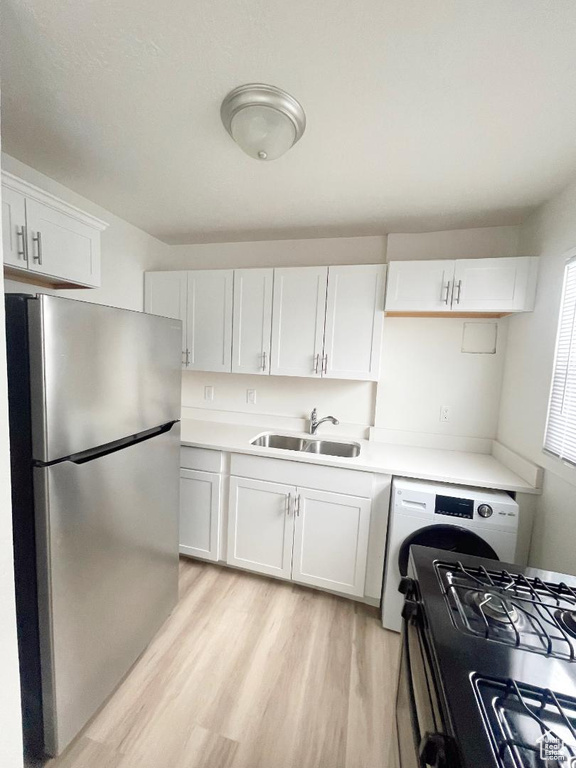Kitchen featuring freestanding refrigerator, a sink, washer / clothes dryer, black gas range, and white cabinets