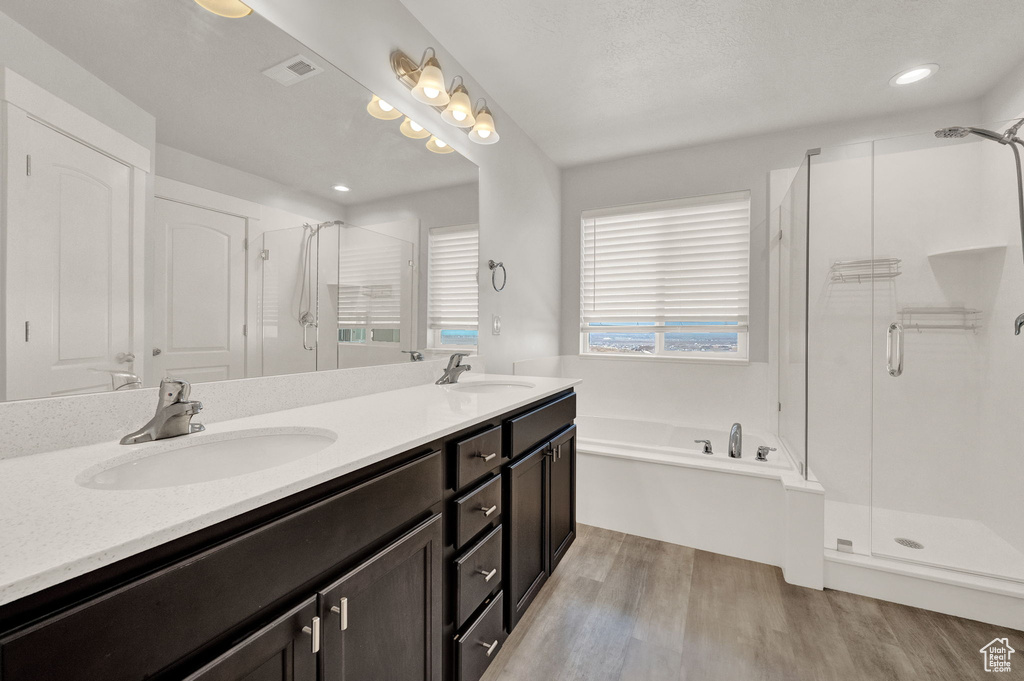 Bathroom with a shower stall, wood finished floors, a bath, double vanity, and recessed lighting