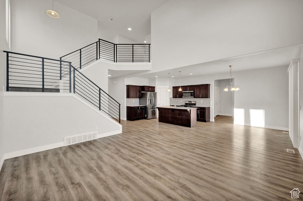 Unfurnished living room featuring light wood-style floors, a high ceiling, stairs, a chandelier, and a sink