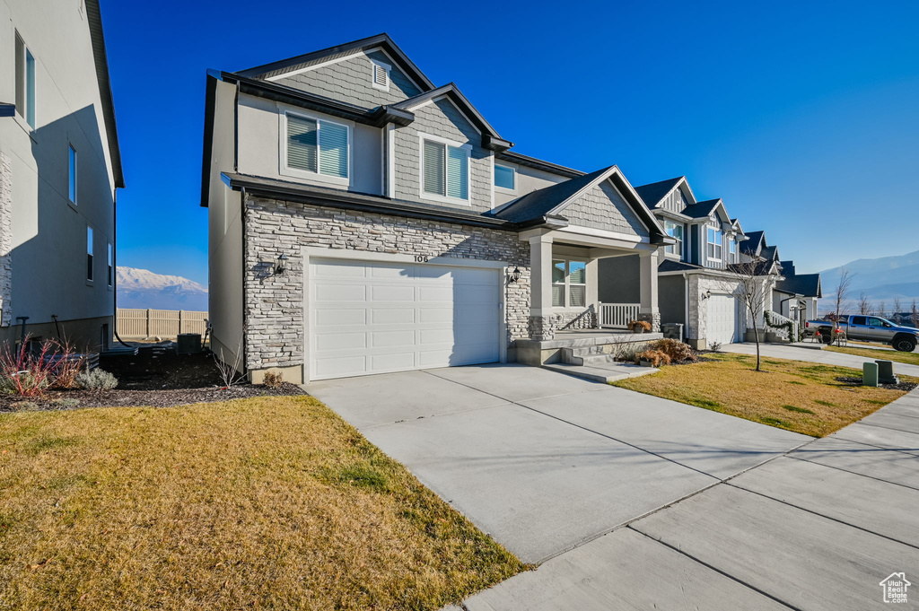 Craftsman house featuring stone siding, concrete driveway, a front yard, a mountain view, and a garage