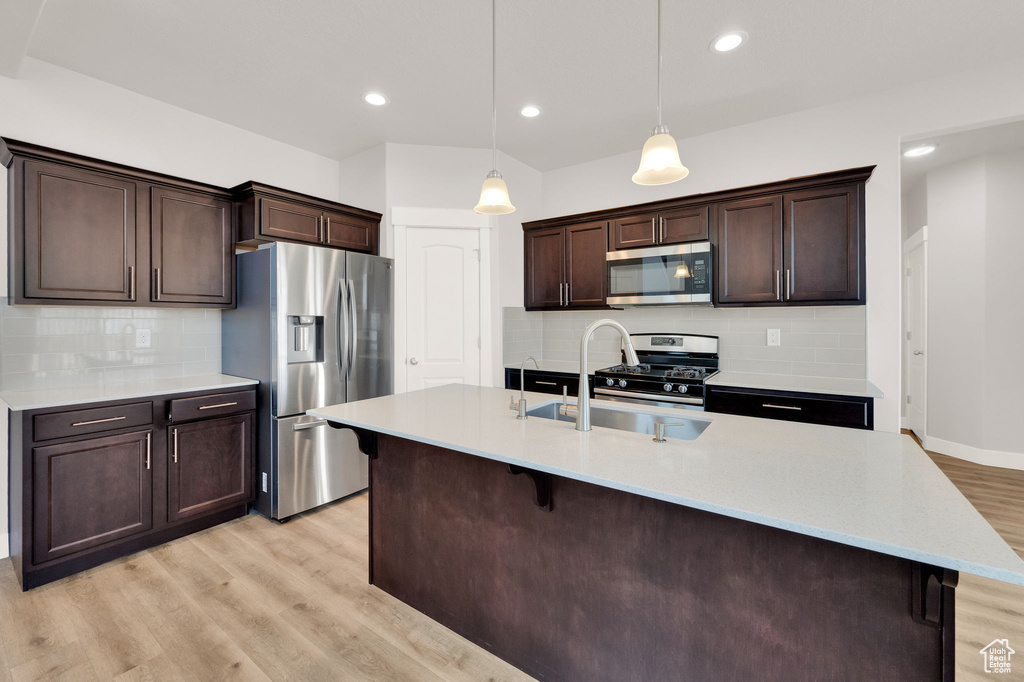 Kitchen with stainless steel appliances, a sink, light wood finished floors, dark brown cabinets, and backsplash