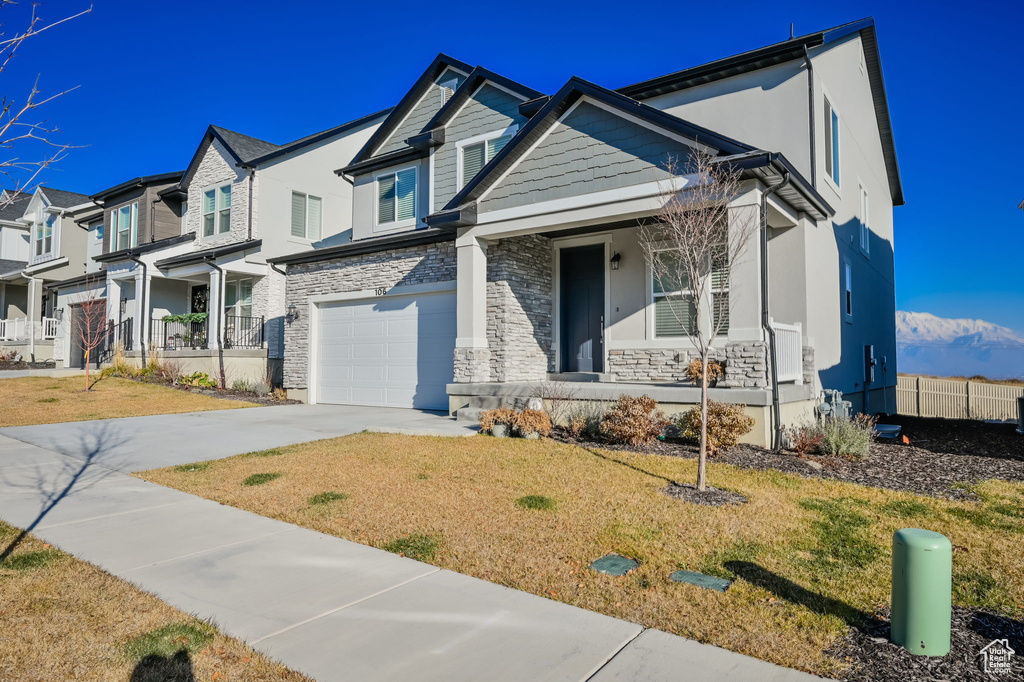 View of front of house featuring a porch, driveway, a garage, stone siding, and stucco siding