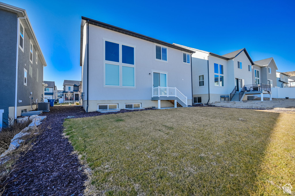 Rear view of property featuring central air condition unit, a residential view, a lawn, stucco siding, and stairway