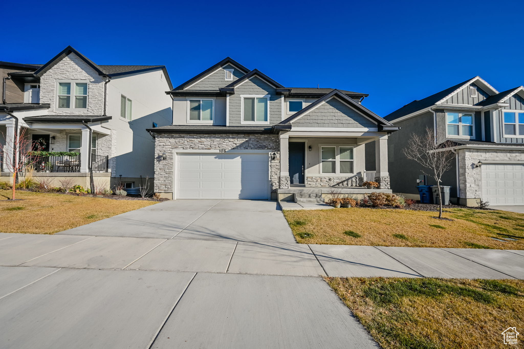 Craftsman-style home featuring covered porch, stone siding, driveway, and a garage