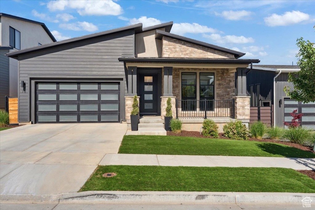 View of front of house with stone siding, a porch, driveway, a garage, and a front yard