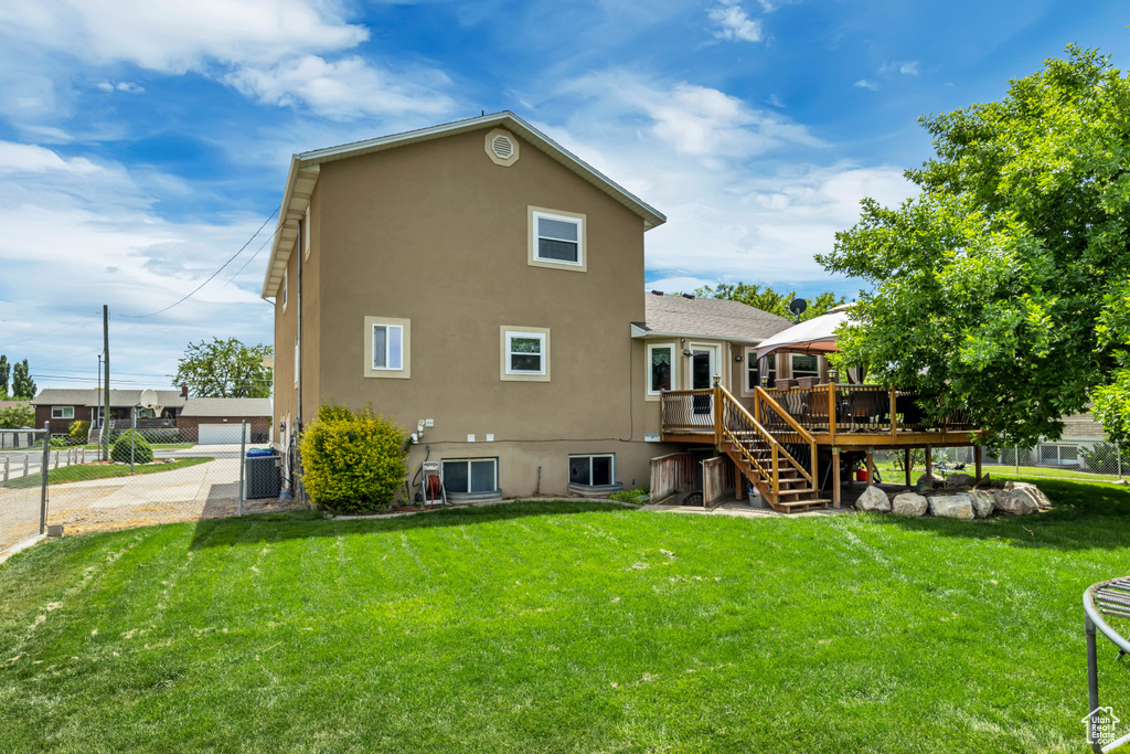 Back of house featuring stucco siding, stairs, a deck, a lawn, and central air condition unit