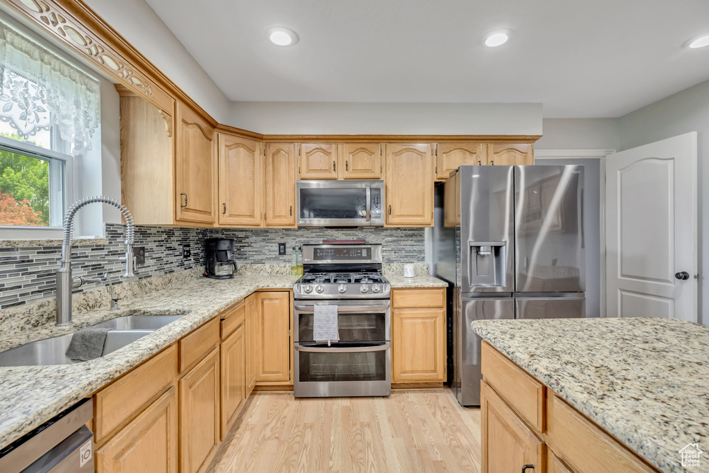 Kitchen with stainless steel appliances, a sink, light wood finished floors, light stone countertops, and recessed lighting