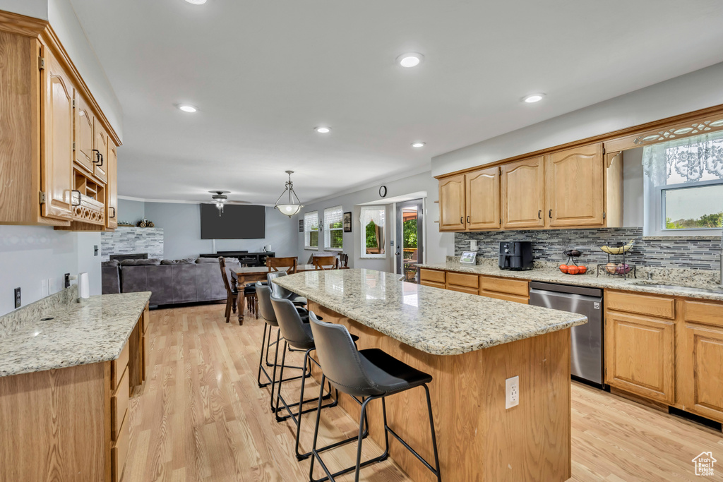 Kitchen featuring stainless steel dishwasher, a center island, open floor plan, a breakfast bar area, and light stone counters
