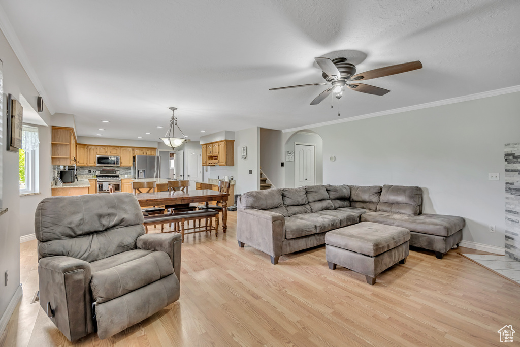 Living room with arched walkways, a ceiling fan, baseboards, light wood finished floors, and crown molding