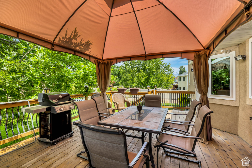 Wooden deck featuring a gazebo, outdoor dining area, and a grill