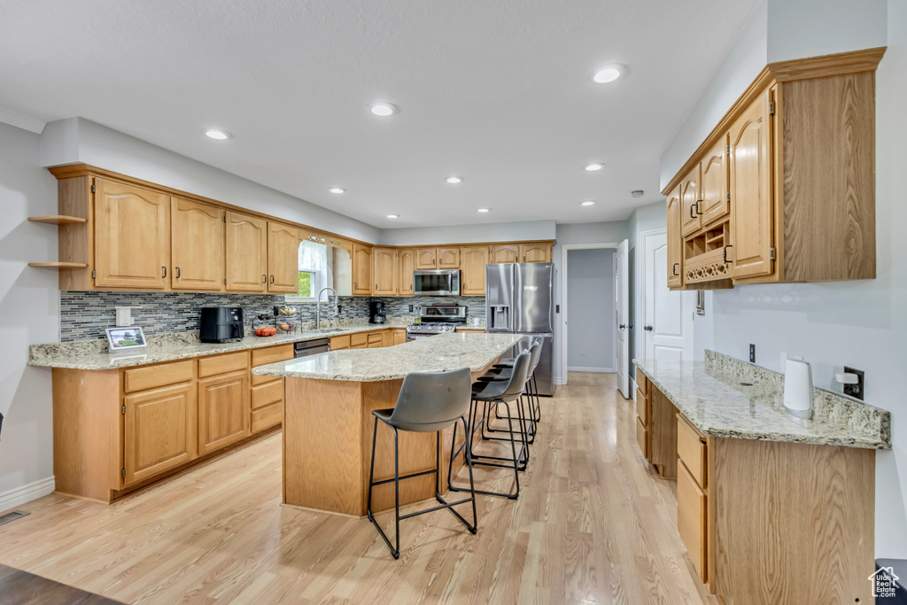 Kitchen featuring appliances with stainless steel finishes, open shelves, a sink, a breakfast bar area, and light wood finished floors
