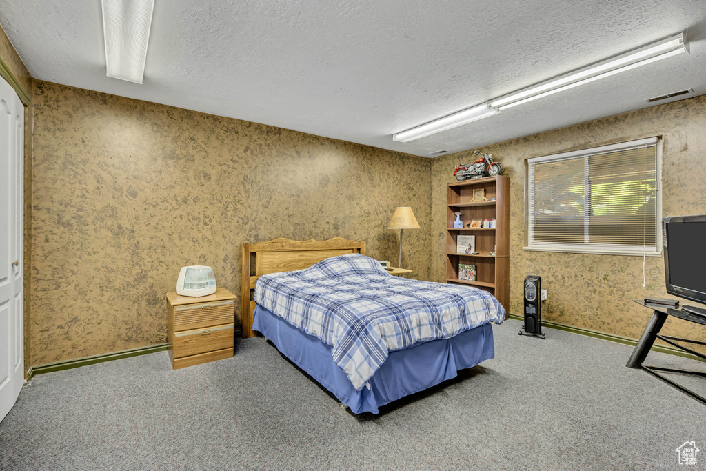 Bedroom featuring a textured ceiling, carpet flooring, wallpapered walls, and baseboards