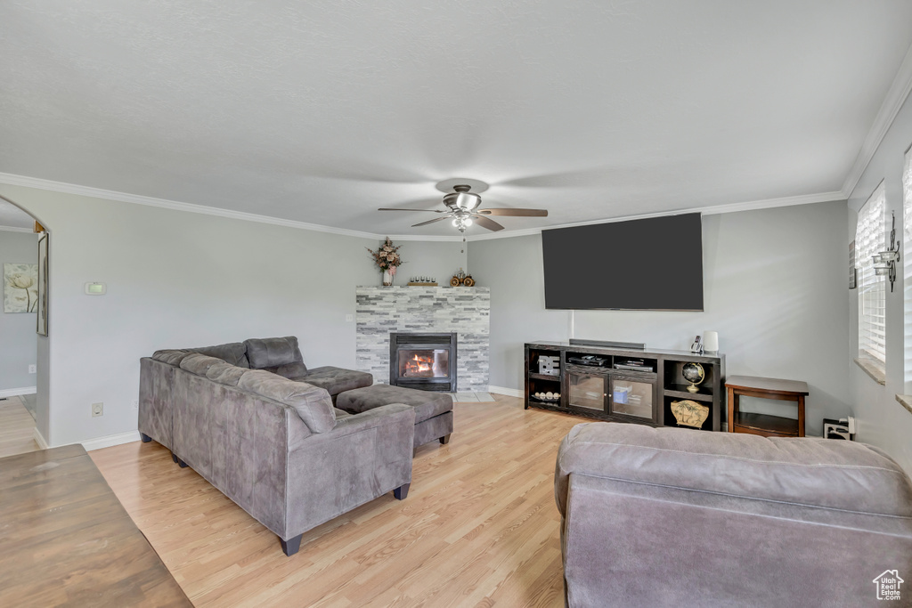 Living room featuring ceiling fan, light wood finished floors, crown molding, a glass covered fireplace, and arched walkways