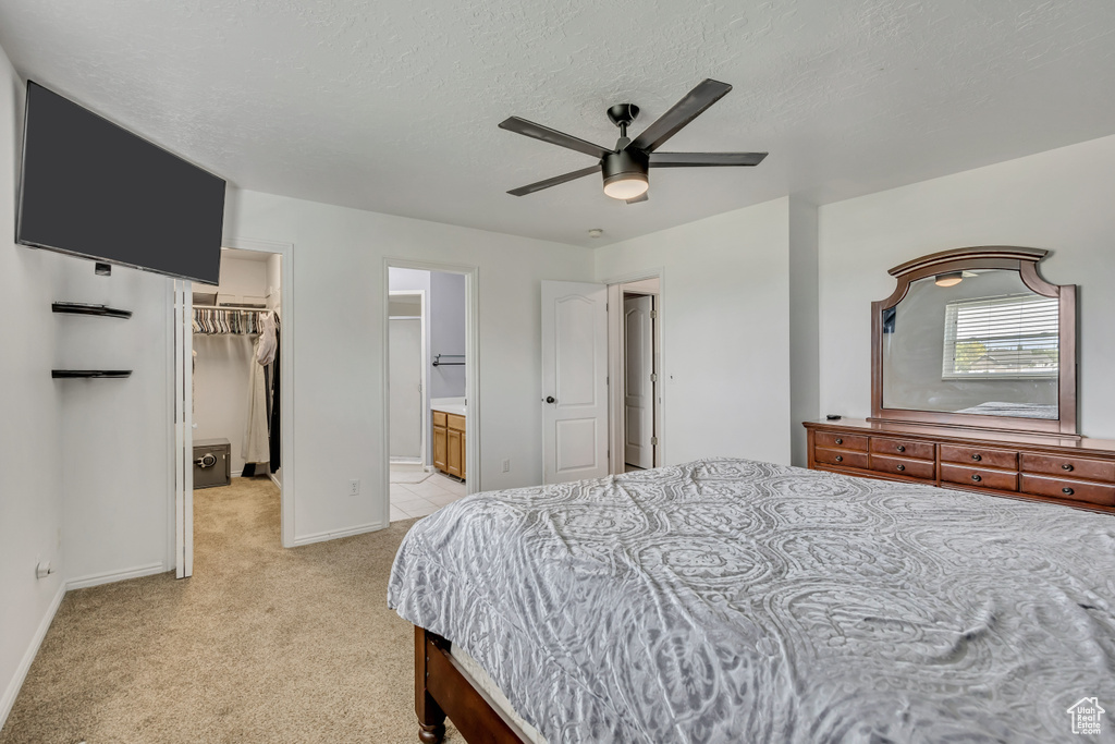 Bedroom featuring light carpet, a walk in closet, baseboards, a textured ceiling, and connected bathroom