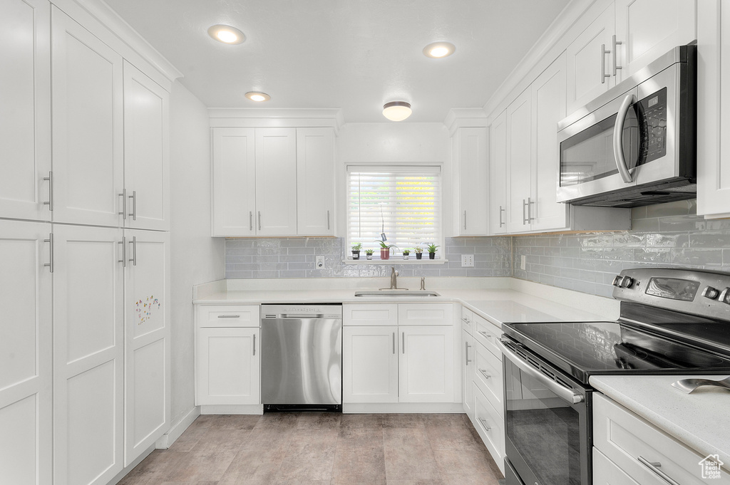 Kitchen featuring appliances with stainless steel finishes, white cabinetry, light wood finished floors, tasteful backsplash, and recessed lighting