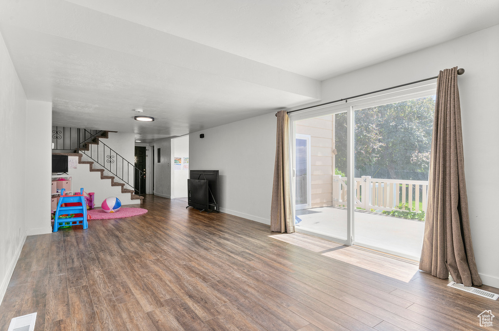 Unfurnished living room featuring wood finished floors, baseboards, and stairway