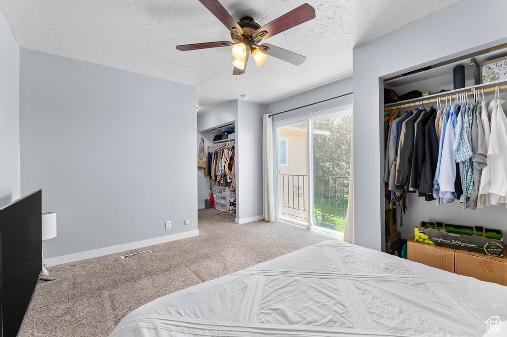 Carpeted bedroom featuring baseboards, a textured ceiling, two closets, and a ceiling fan