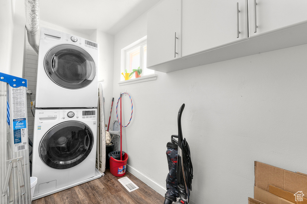 Laundry area with estacked washer and dryer, wood finished floors, cabinet space, and baseboards