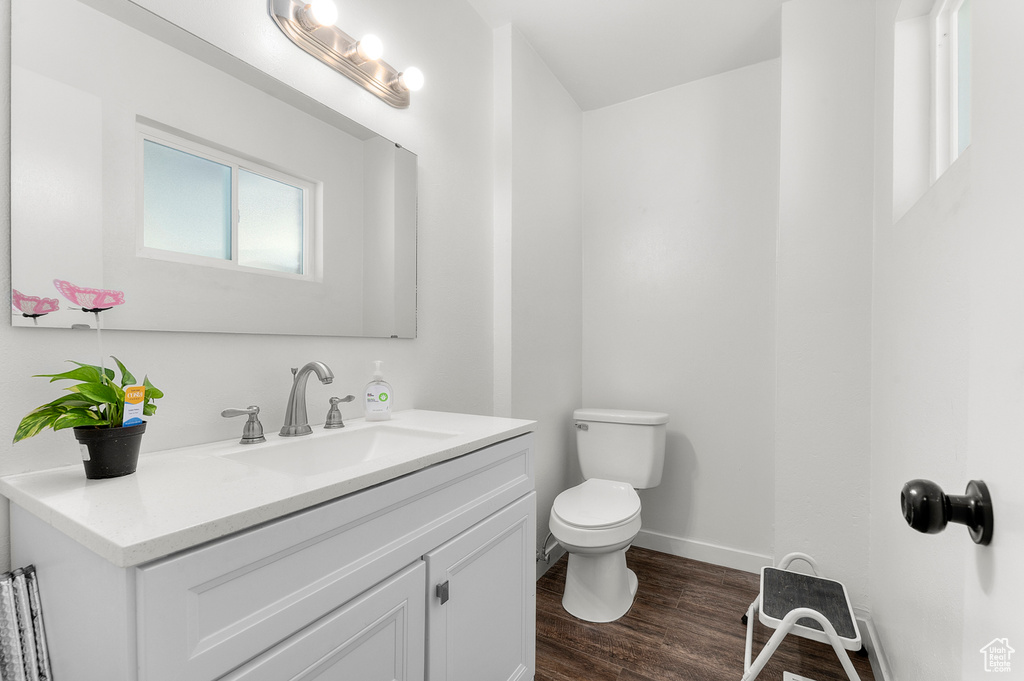 Half bathroom featuring toilet, vanity, wood finished floors, and baseboards