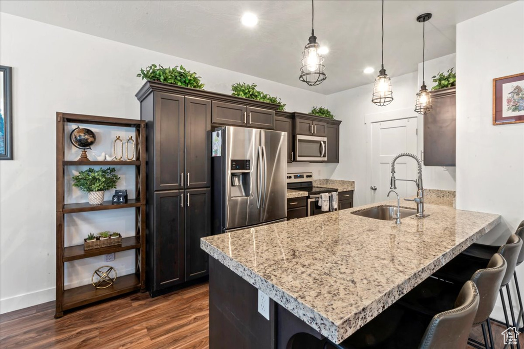 Kitchen with appliances with stainless steel finishes, a sink, dark brown cabinets, dark wood-style flooring, and a peninsula