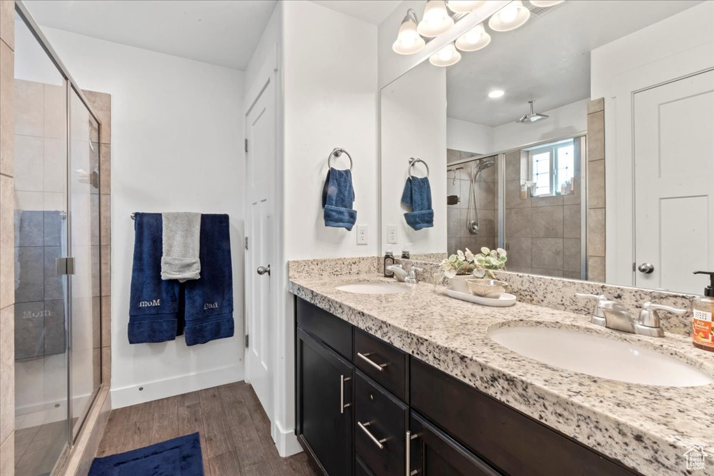 Full bath with a stall shower, double vanity, wood finished floors, and baseboards