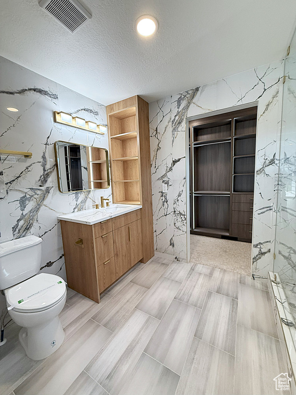 Full bathroom featuring toilet, vanity, a textured ceiling, a marble finish shower, and stone wall