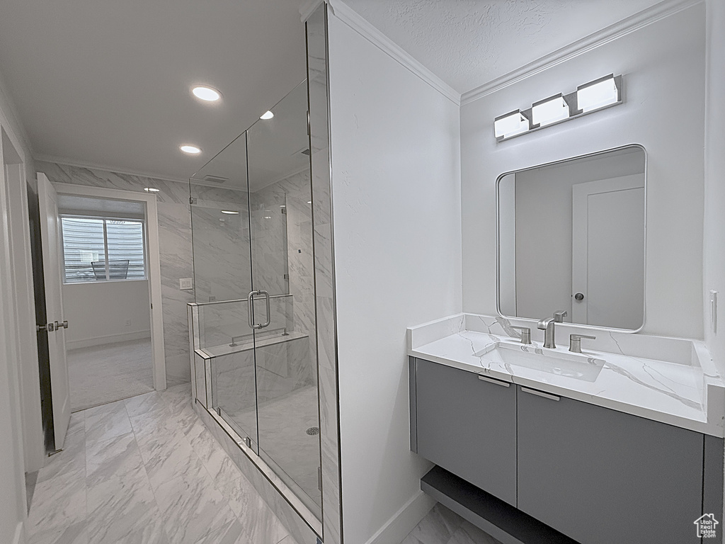Full bath with marble look tile flooring, ornamental molding, a marble finish shower, vanity, and baseboards