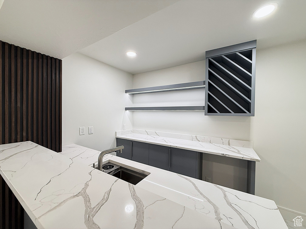 Kitchen with open shelves, a sink, light stone counters, and recessed lighting