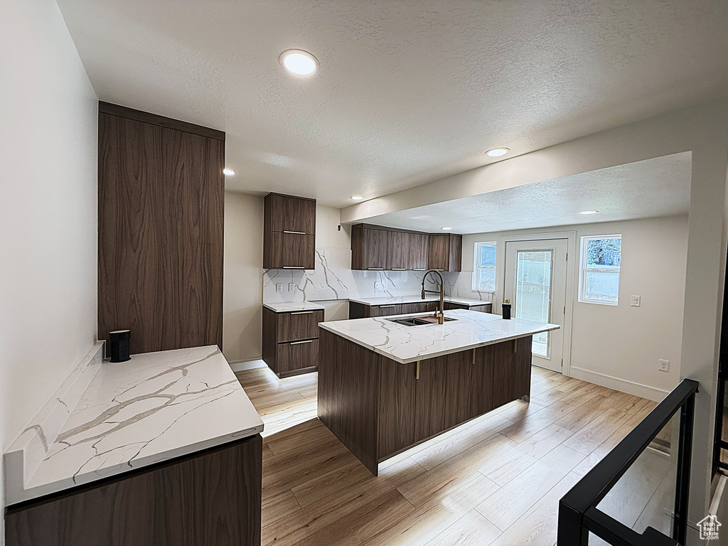 Kitchen featuring a sink, a kitchen island with sink, light wood finished floors, dark brown cabinets, and a textured ceiling