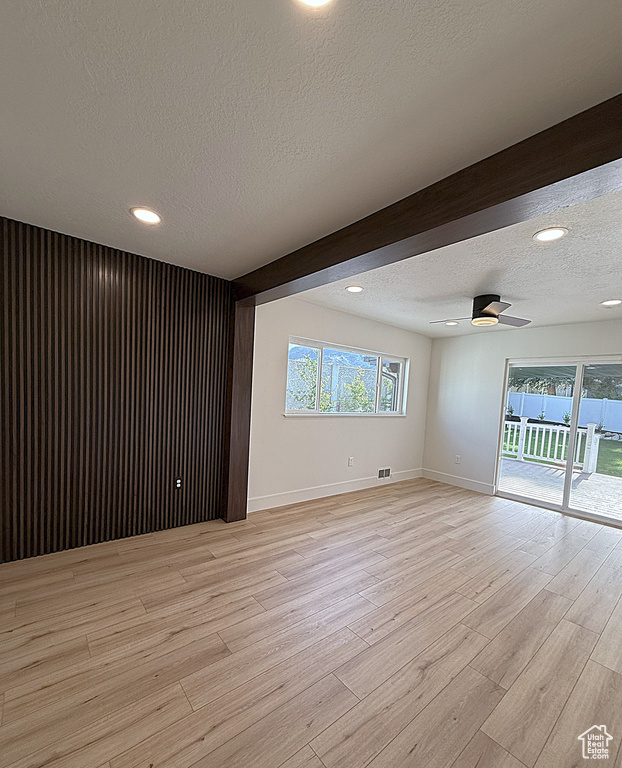 Empty room with a textured ceiling, light wood-style floors, ceiling fan, baseboards, and plenty of natural light