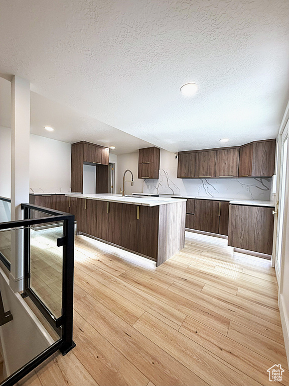 Kitchen featuring light wood finished floors, light countertops, a textured ceiling, modern cabinets, and a kitchen island with sink