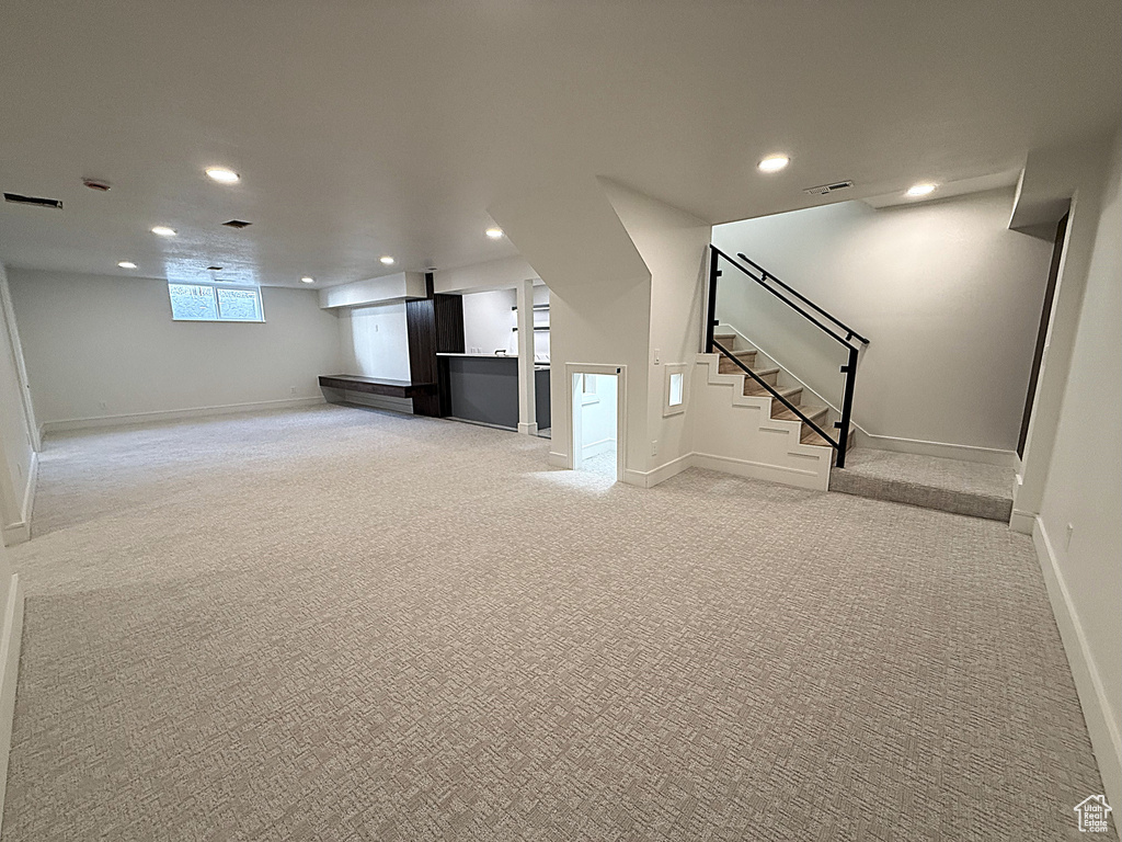 Unfurnished living room with recessed lighting, light carpet, stairs, and baseboards