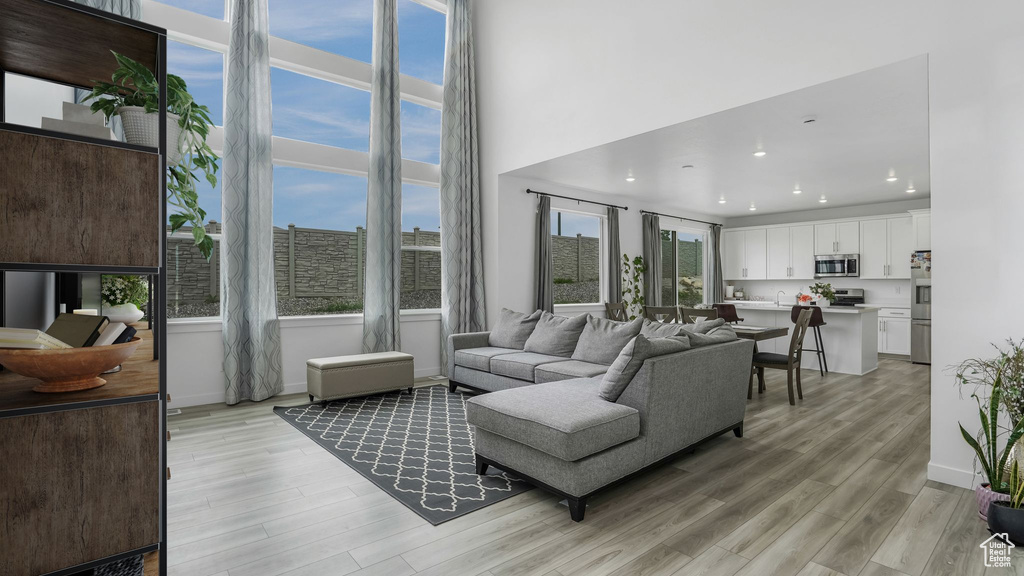 Living room with light wood finished floors, recessed lighting, baseboards, and a high ceiling