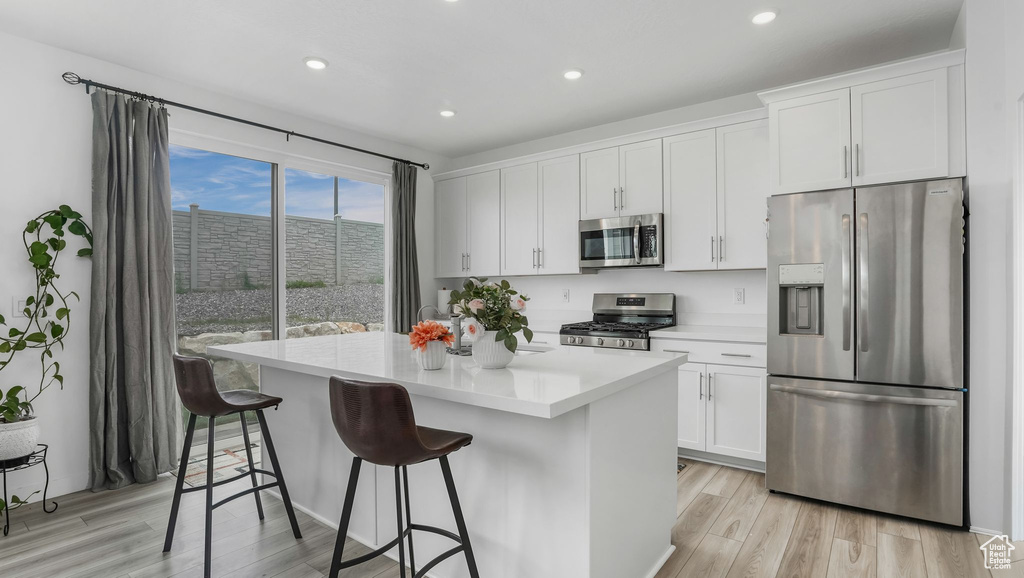 Kitchen featuring stainless steel appliances, a kitchen island with sink, light wood-style flooring, white cabinets, and a breakfast bar area