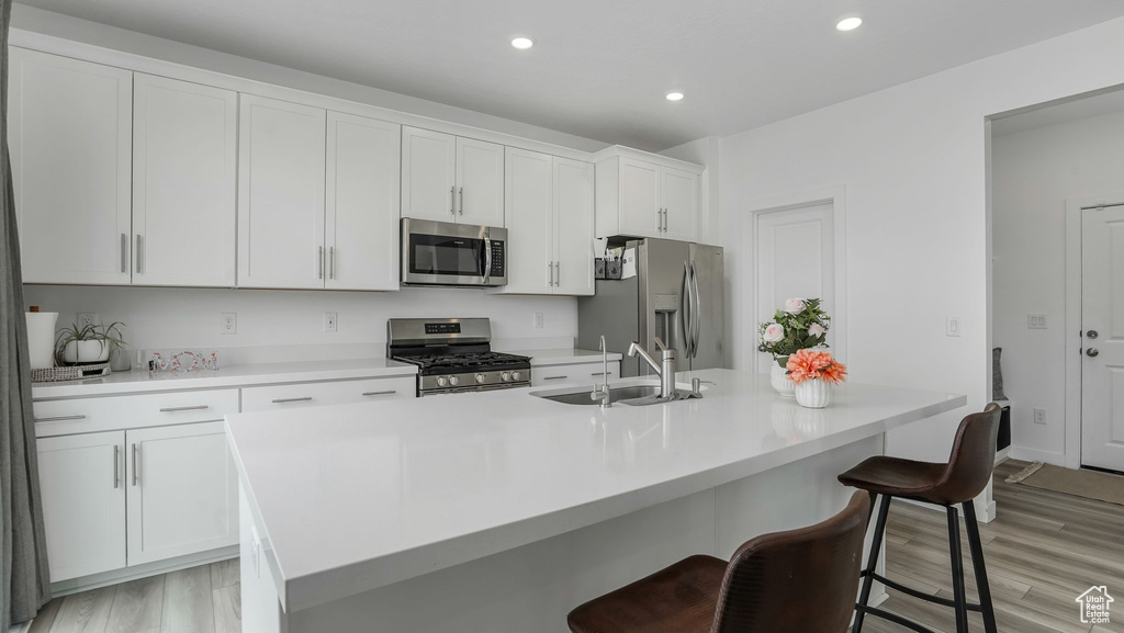 Kitchen with stainless steel appliances, a sink, light wood-style flooring, white cabinetry, and a kitchen island with sink