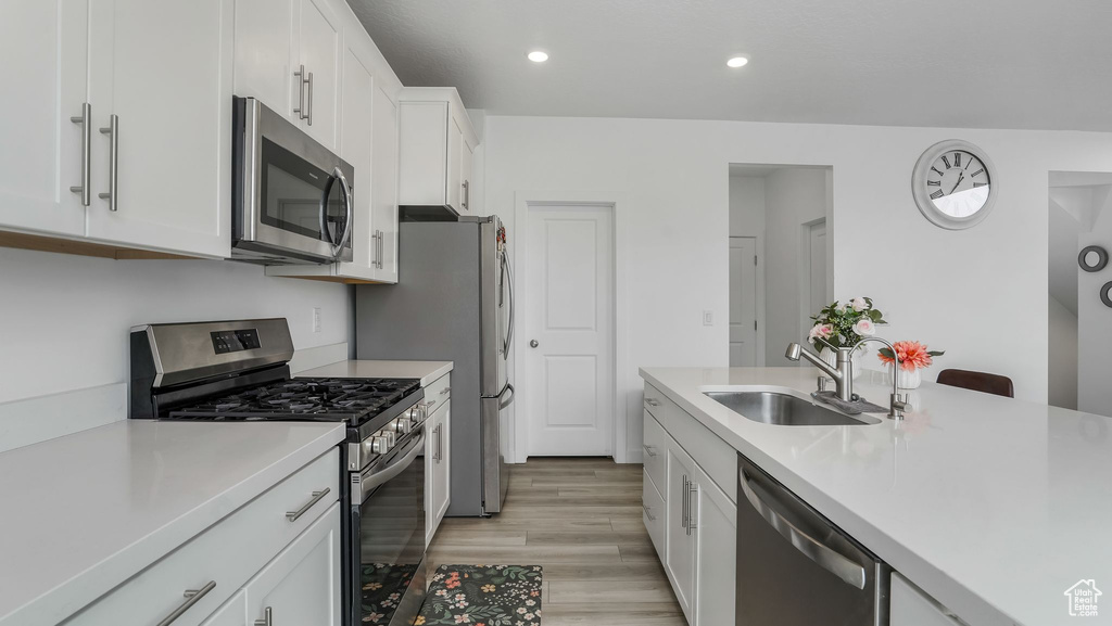 Kitchen with appliances with stainless steel finishes, a sink, light countertops, light wood-style flooring, and white cabinets