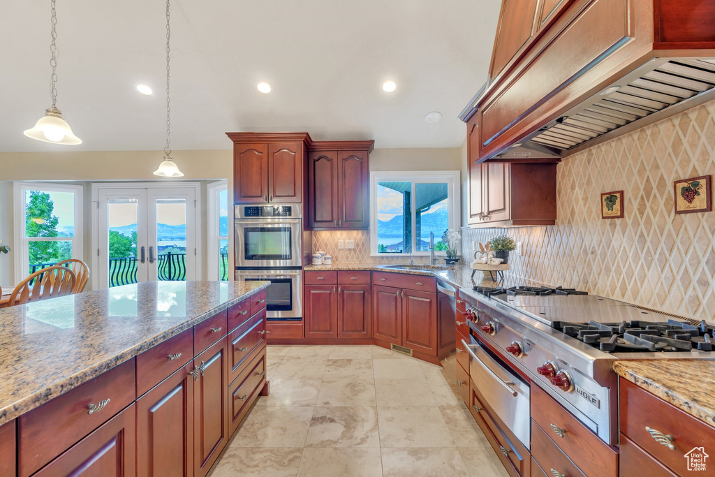Kitchen with custom range hood, appliances with stainless steel finishes, a warming drawer, backsplash, and light stone countertops