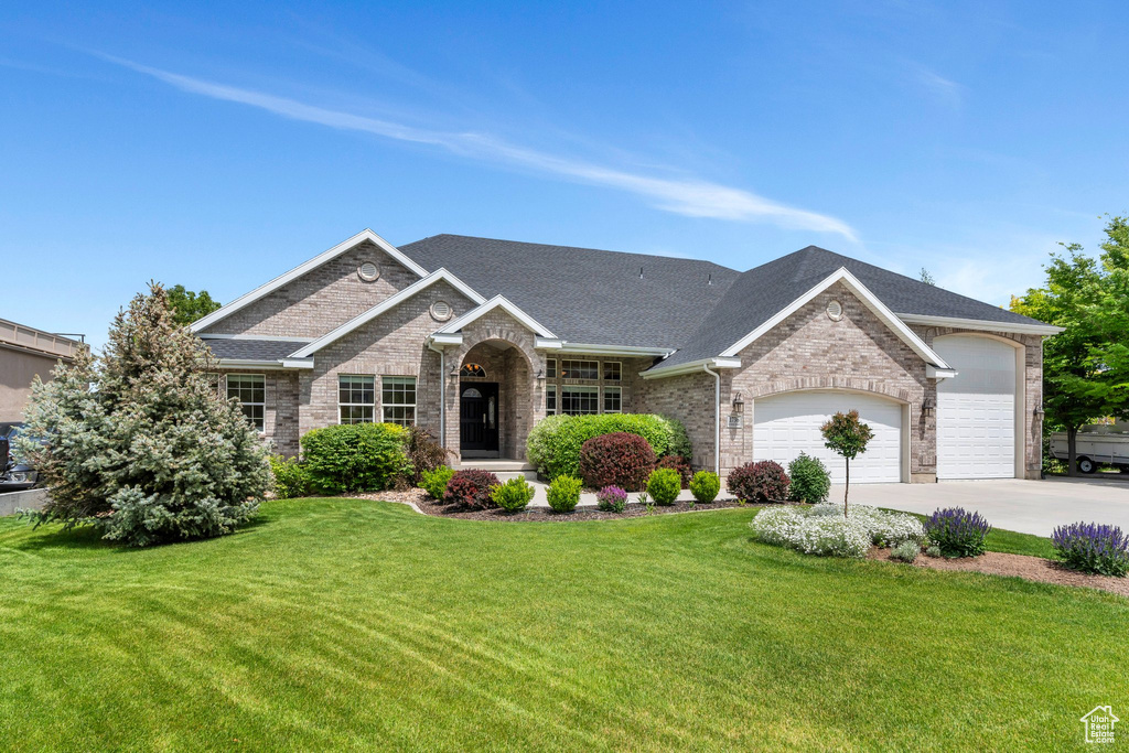 View of front of property with a garage, brick siding, a front lawn, and driveway