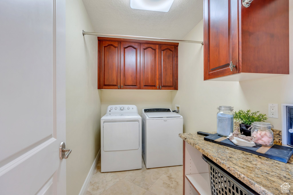 Laundry room featuring cabinet space, washer and clothes dryer, baseboards, and a textured ceiling