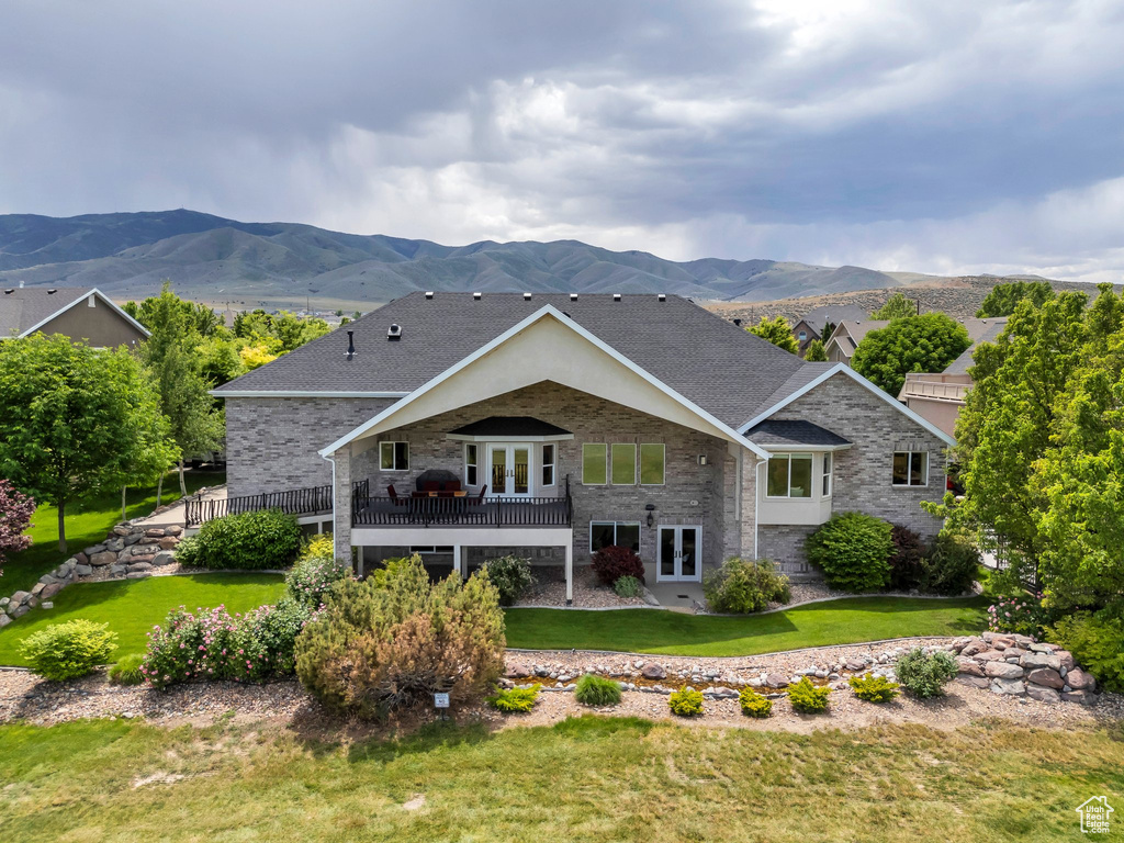 Rear view of property featuring french doors, stone siding, a mountain view, a yard, and roof with shingles