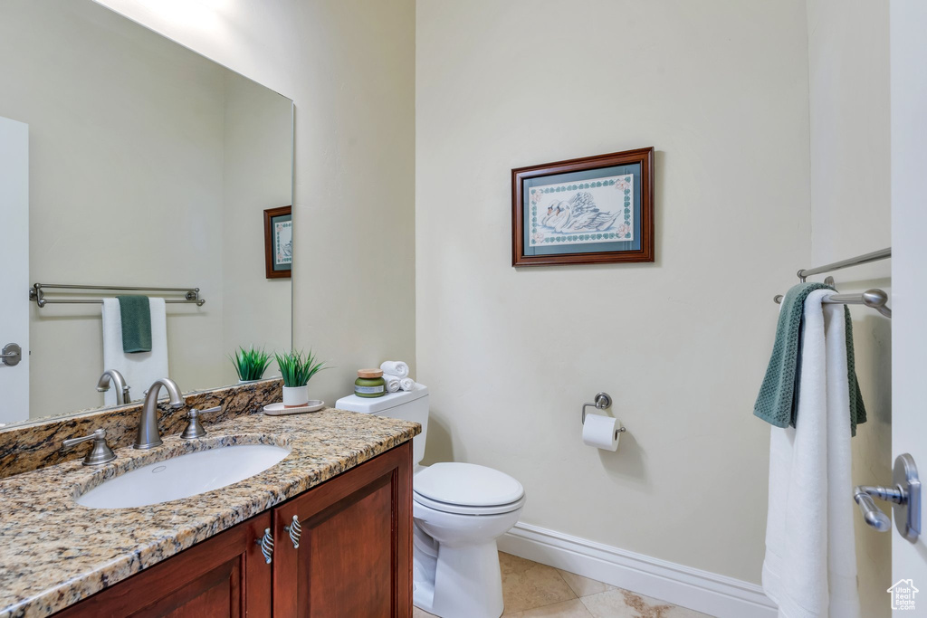 Half bath with baseboards, vanity, toilet, and tile patterned floors